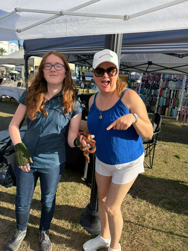 Michelle Sawyer with a market visitor at the Shooting Star Products stand at Jax Beach Market featuring natural home products and candles